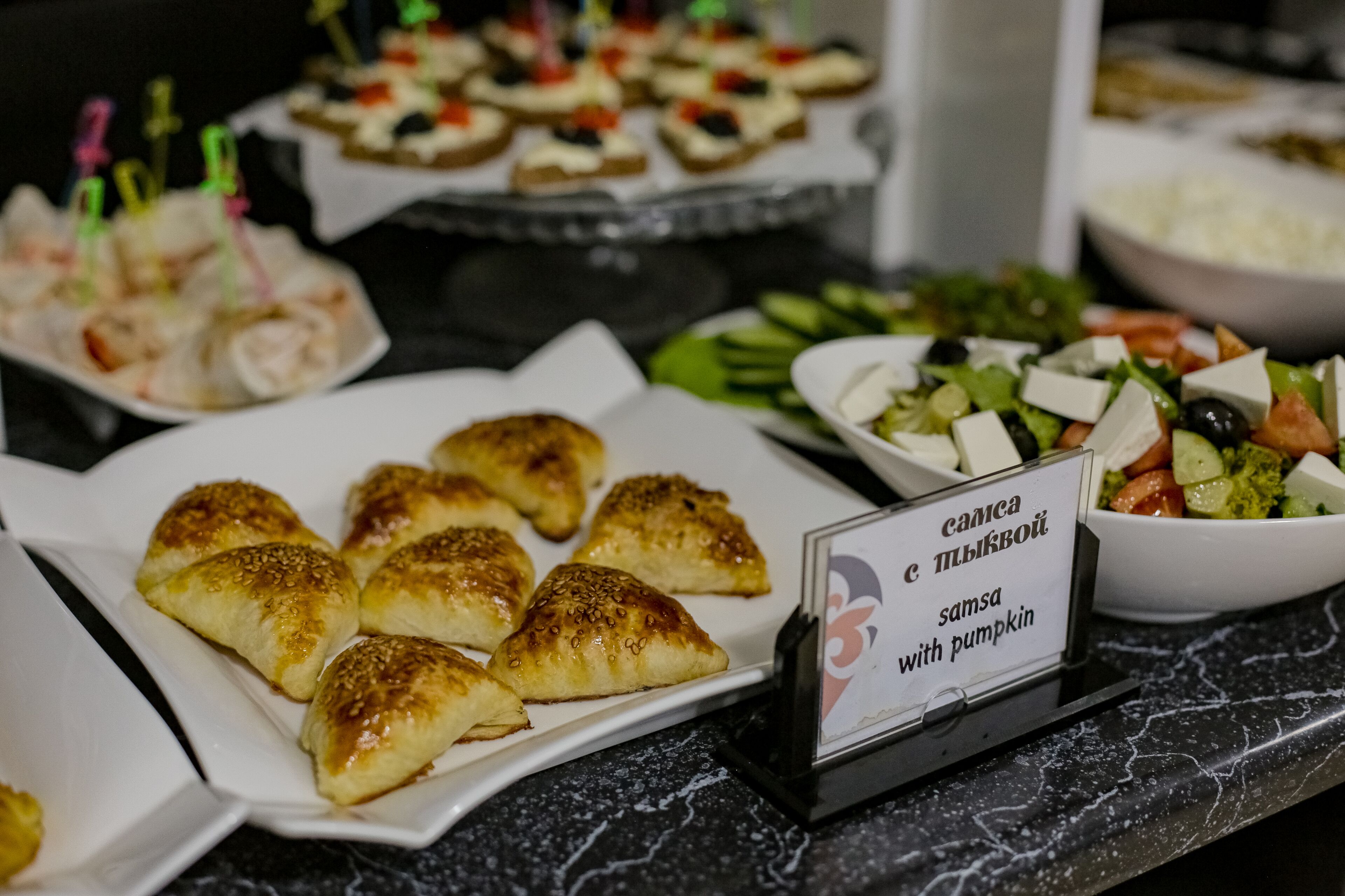 A buffet table with various food items including samosas, a salad, and other dishes.