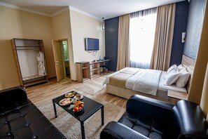A hotel room with a bed, a desk with a chair, a TV, a wardrobe, and a coffee table with breakfast items.