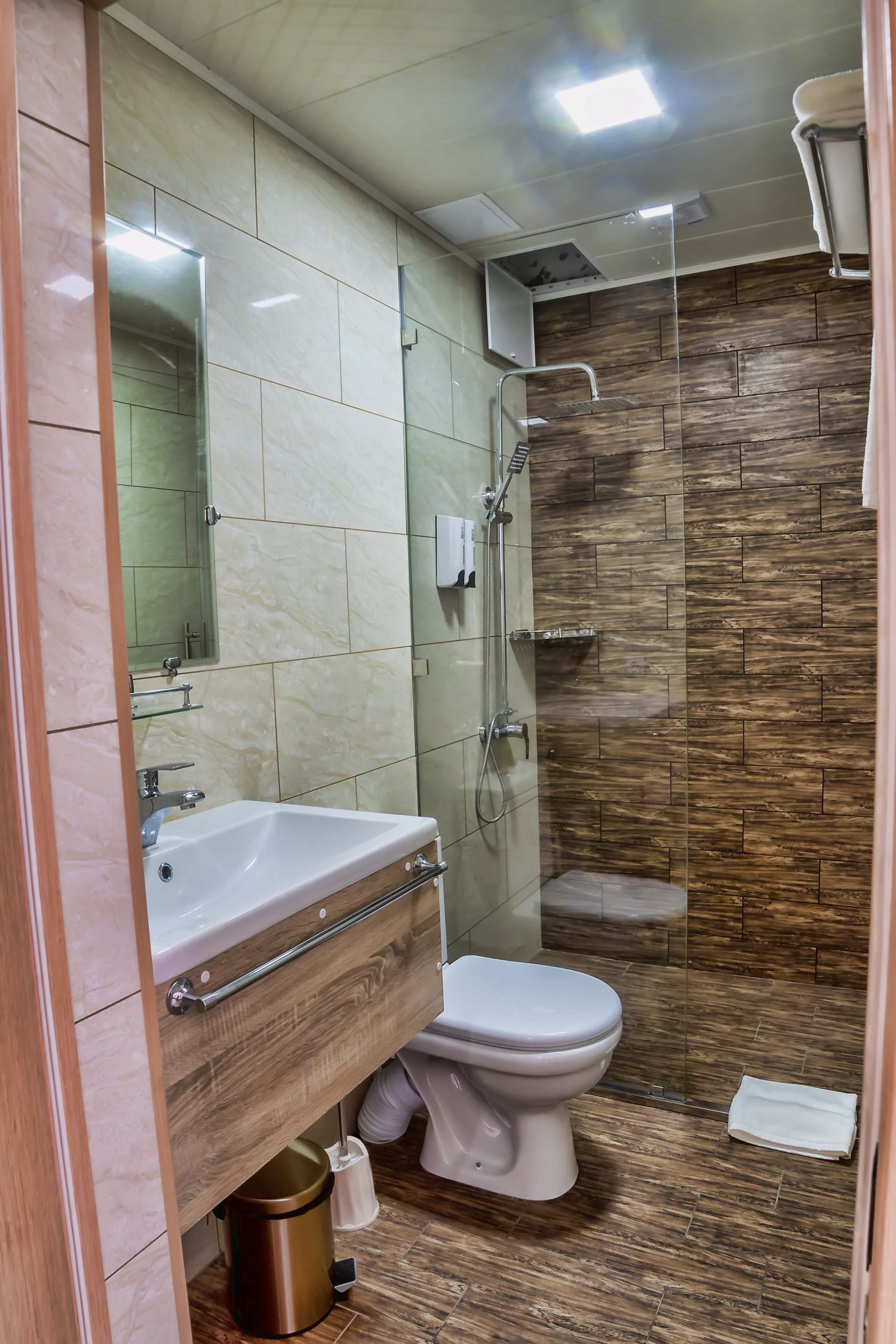Un baño con tocador de mármol, inodoro, ducha con puerta de vidrio y suelo de madera.