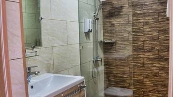 Un baño con tocador de mármol, inodoro, ducha con puerta de vidrio y suelo de madera.