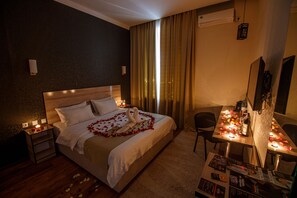 A hotel room with a bed, bedside tables with candles, a desk with a mirror, and a TV.