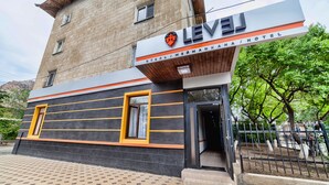 A hotel with a modern facade, featuring a prominent sign with the name 'LEVEL' and 'HOTEL' in large letters. The building has a brick exterior with horizontal lines and a wooden overhang above the entrance. - Level Hotel (Osh)