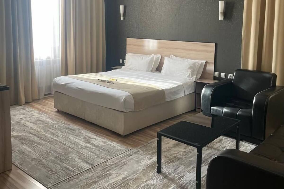 A hotel room with a large bed, a black leather chair, a small table, and a nightstand.