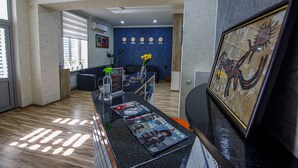 A reception area with a reception desk, a clock, a vase with flowers, and a framed picture on the wall. - Level Hotel (Osh)