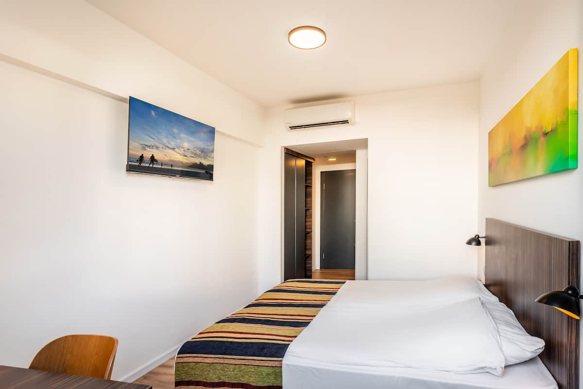 Une chambre d’hôtel équipée d’un lit, d’un bureau, d’une chaise, d’un tableau au mur et d’un appareil de climatisation.