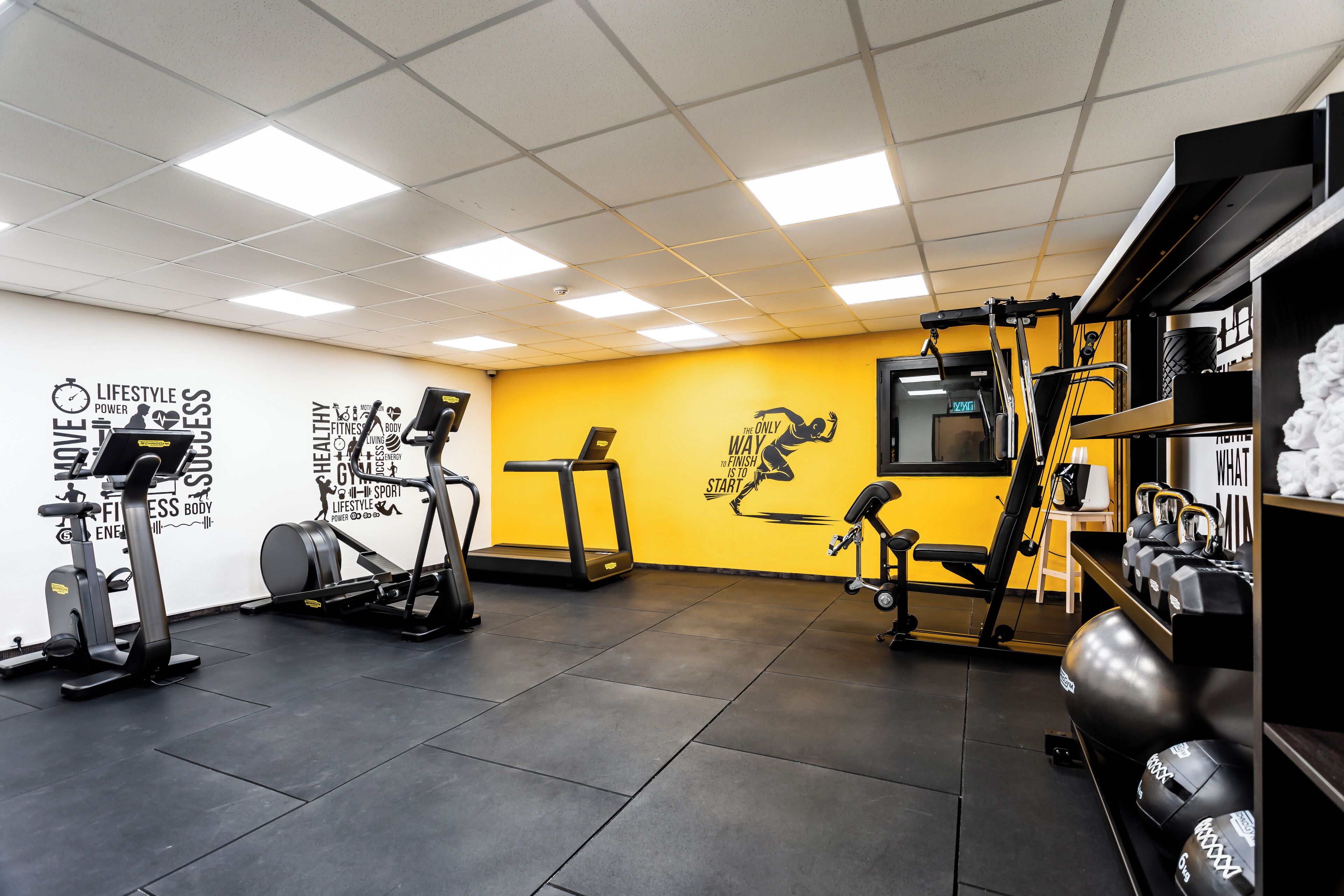 Une salle de sport équipée de matériel d’exercice, agrémentée d’œuvres d’art murales inspirantes et d’un mur d’accent jaune.