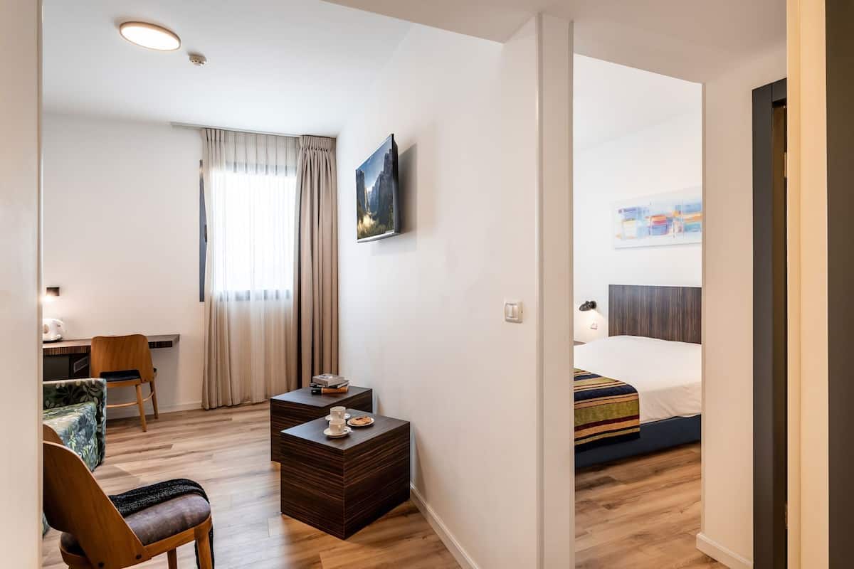 Une chambre d’hôtel avec un lit, un bureau, une chaise, une petite table sur laquelle se trouve un plateau avec divers objets, et un tableau accroché au mur.