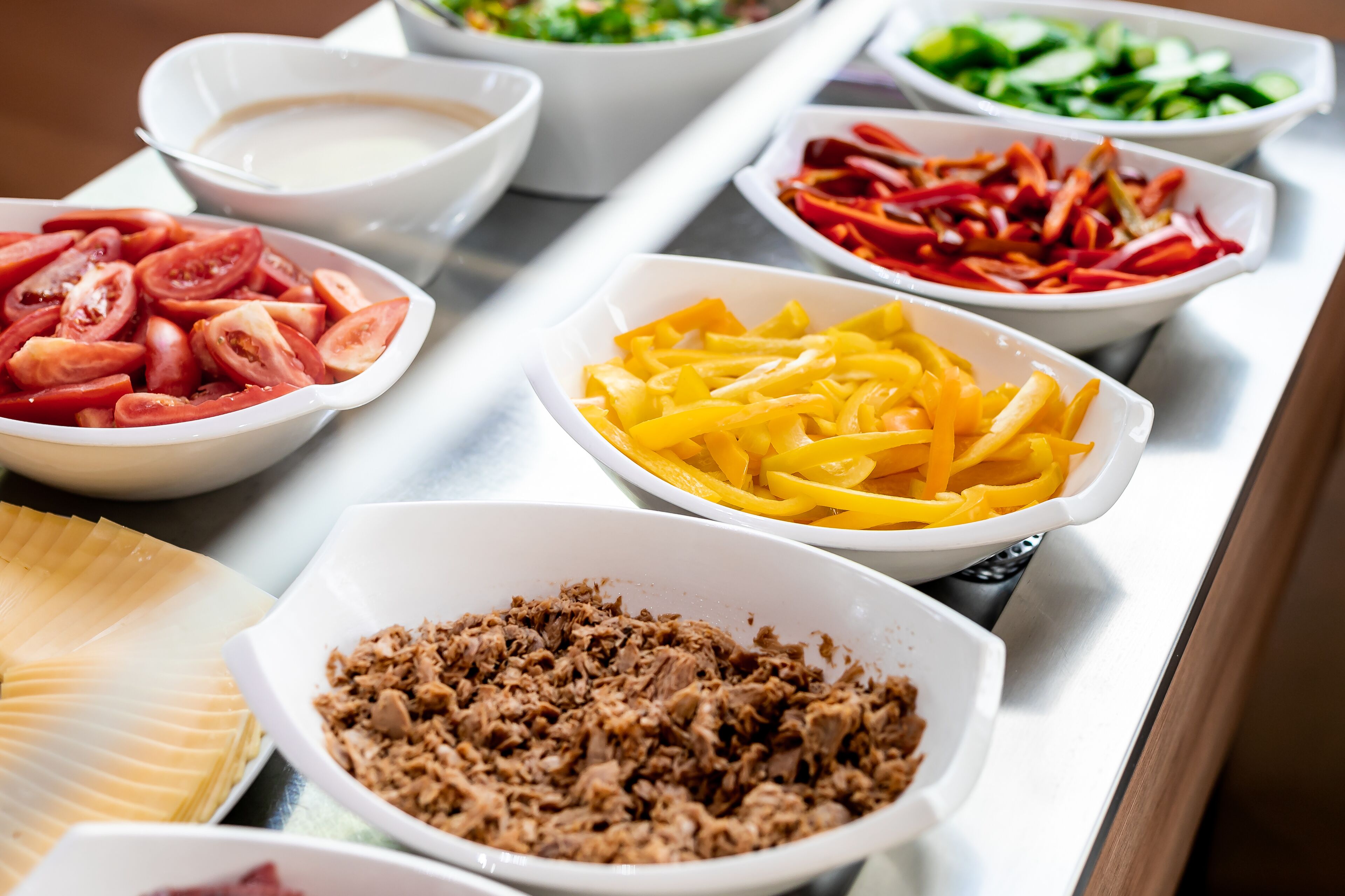Une table de buffet proposant divers aliments, notamment des tomates en tranches, du fromage râpé et de la viande.