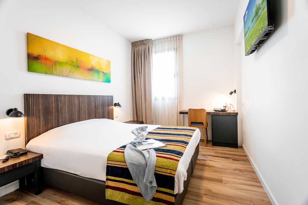 Une chambre d’hôtel avec un grand lit, un bureau avec une lampe, une petite kitchenette et un tableau au mur.