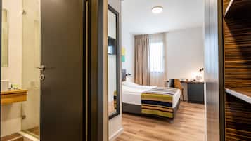Una habitación de hotel moderna con piso de madera, una cama con manta a rayas, una mesita de noche, un escritorio y una ventana con cortinas.