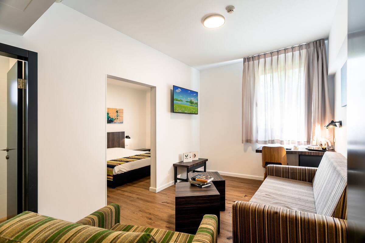 Une chambre d’hôtel moderne équipée d’un lit, d’un canapé, d’une petite table et d’un bureau avec une lampe.