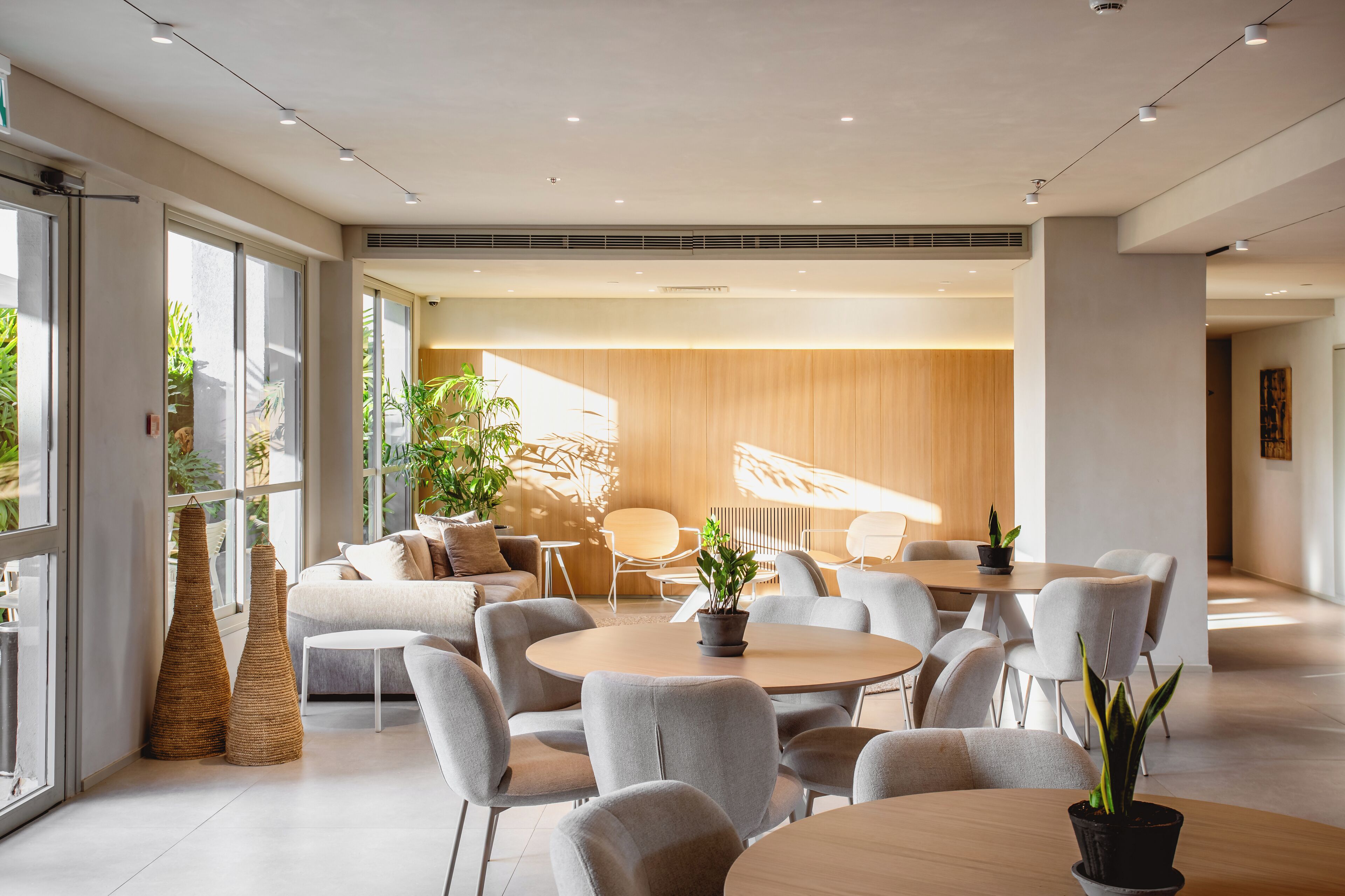 A modern interior with round tables and grey chairs, large windows, and indoor plants.
