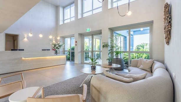 Ein moderner Empfangsbereich mit einer Rezeption, einer Sitzecke und großen Fenstern mit Blick auf Grünflächen.