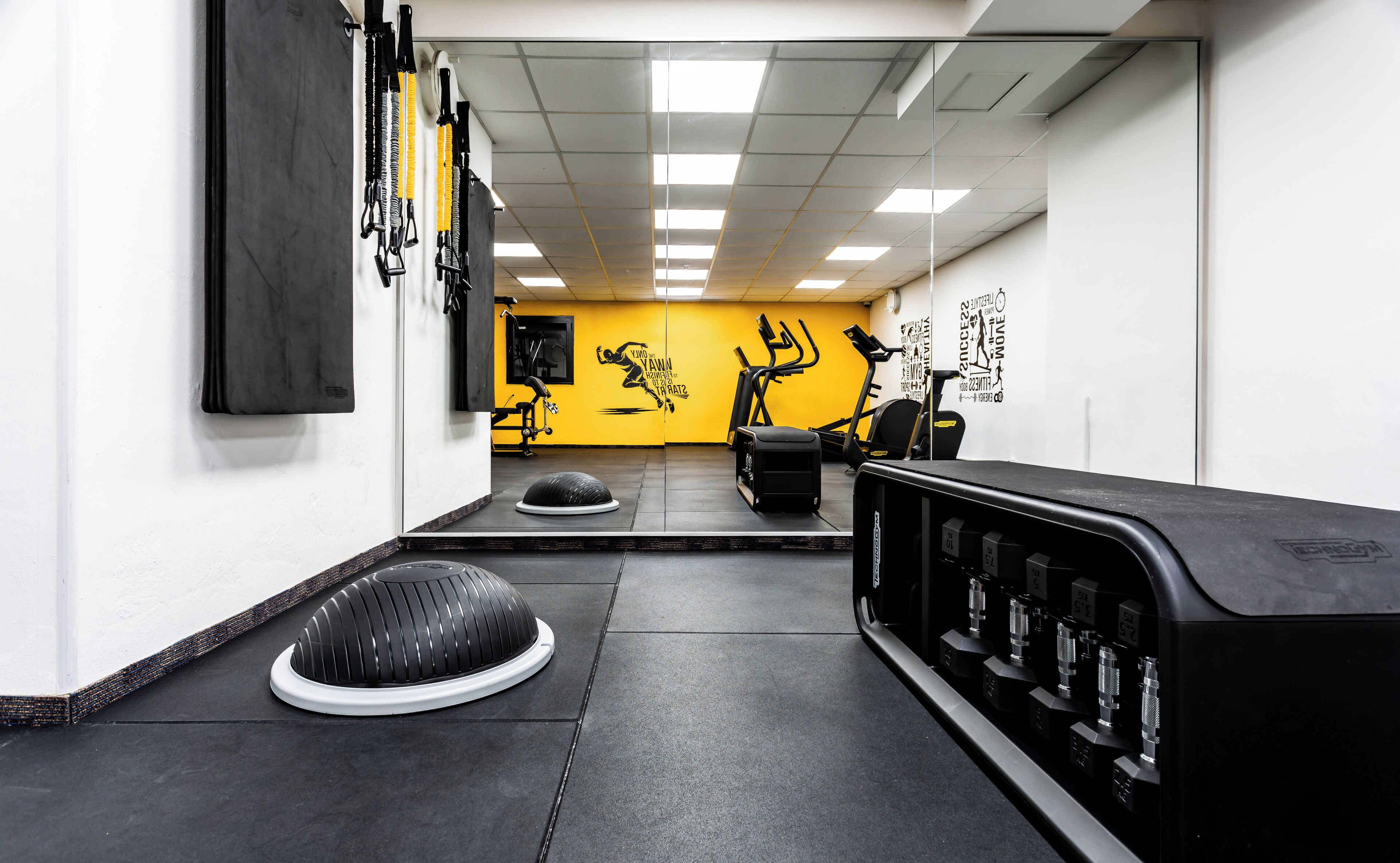 Et fitnesscenter med træningsudstyr, et spejl og motiverende plakater.