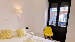 A hotel room with a bed, a yellow chair, a swan-shaped towel, and a window with a view of buildings. - CH Arriaza II (Madrid)
