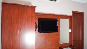 A room with a wooden wardrobe, a flat-screen TV mounted on the wall, and a small wooden table with a glass top.