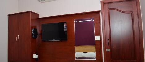 A bedroom with a wooden wardrobe, a built-in TV, a bedside table, and a door.