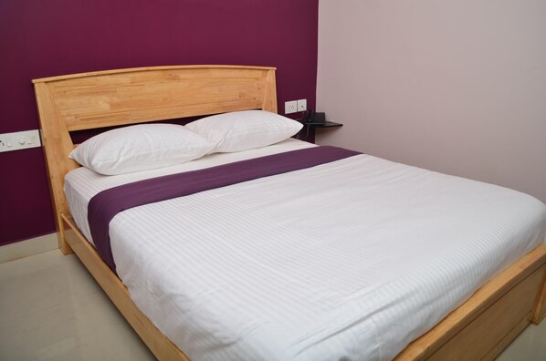 A single bed with a wooden headboard, white bedding, and a purple throw blanket.