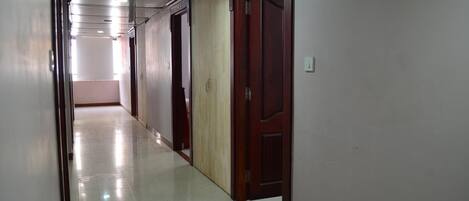 Un pasillo largo y estrecho con suelo de baldosas brillantes y puertas de madera a un lado.