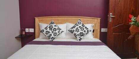 A neatly made bed with a wooden headboard, two patterned pillows, and a purple bedspread.