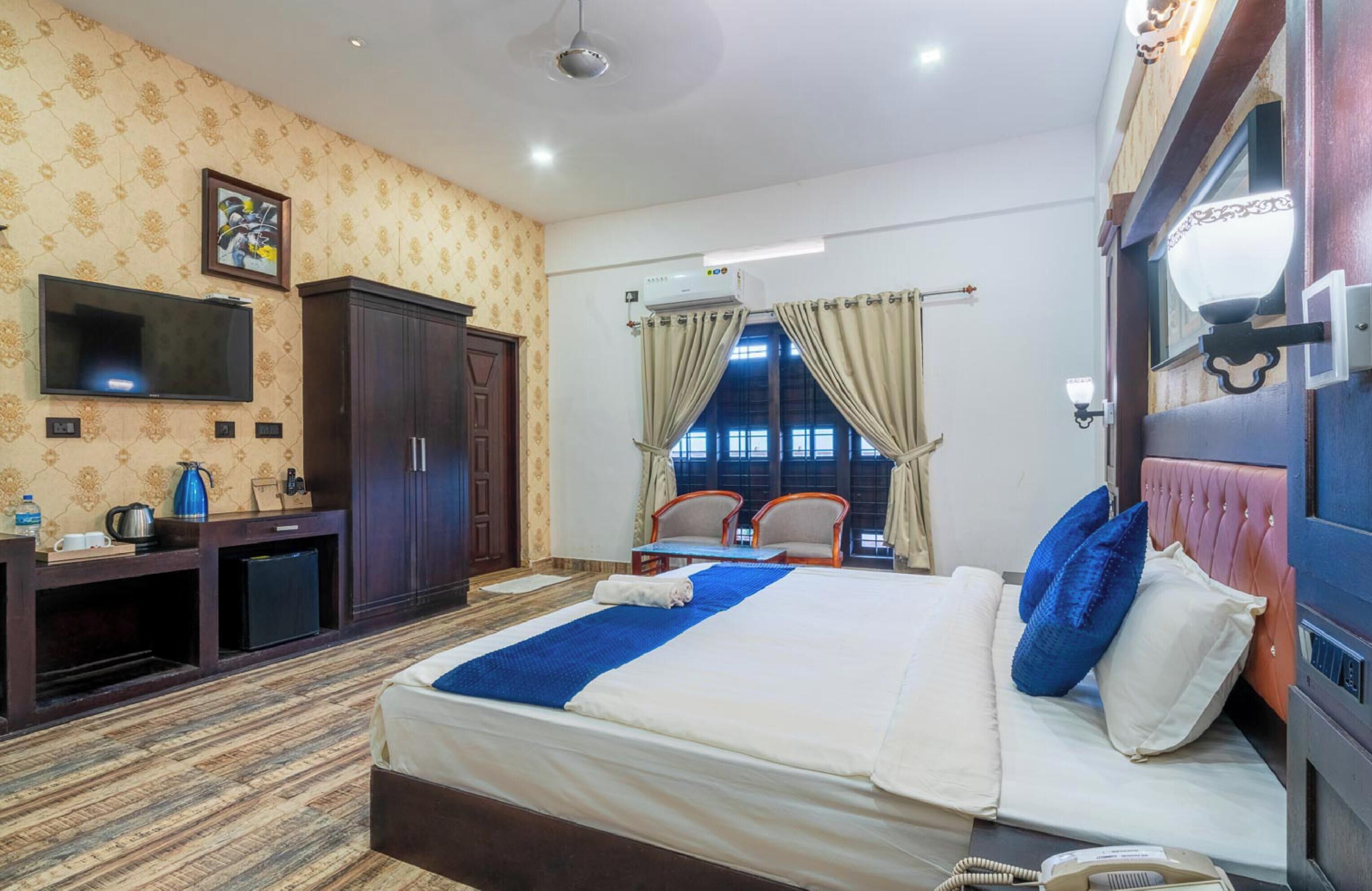 Habitación de hotel con una cama grande, un televisor montado en la pared, un armario, un escritorio con silla y una ventana con cortinas.