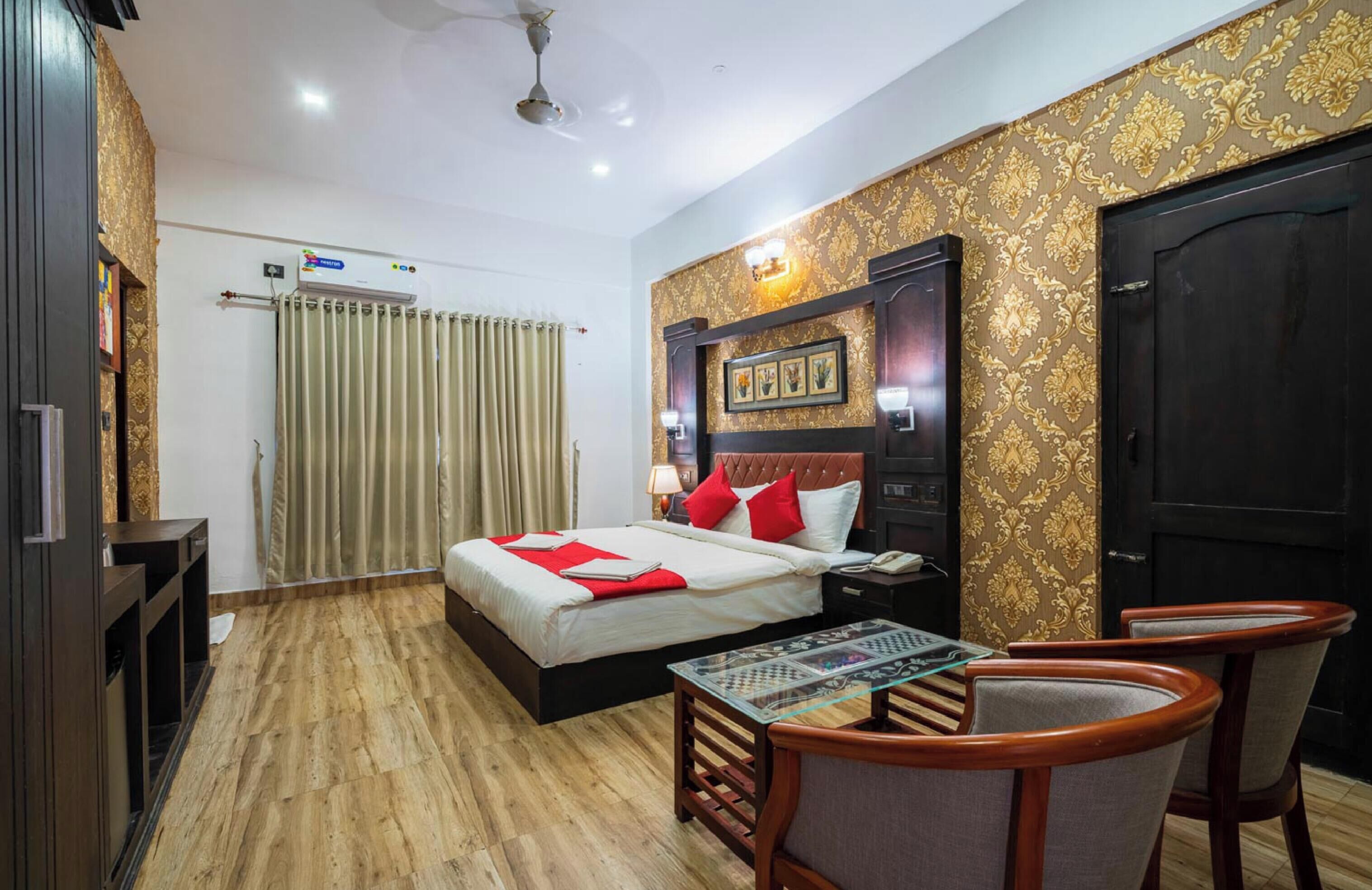 Une chambre d’hôtel avec un lit, un bureau, deux chaises, un ventilateur de plafond et une porte.