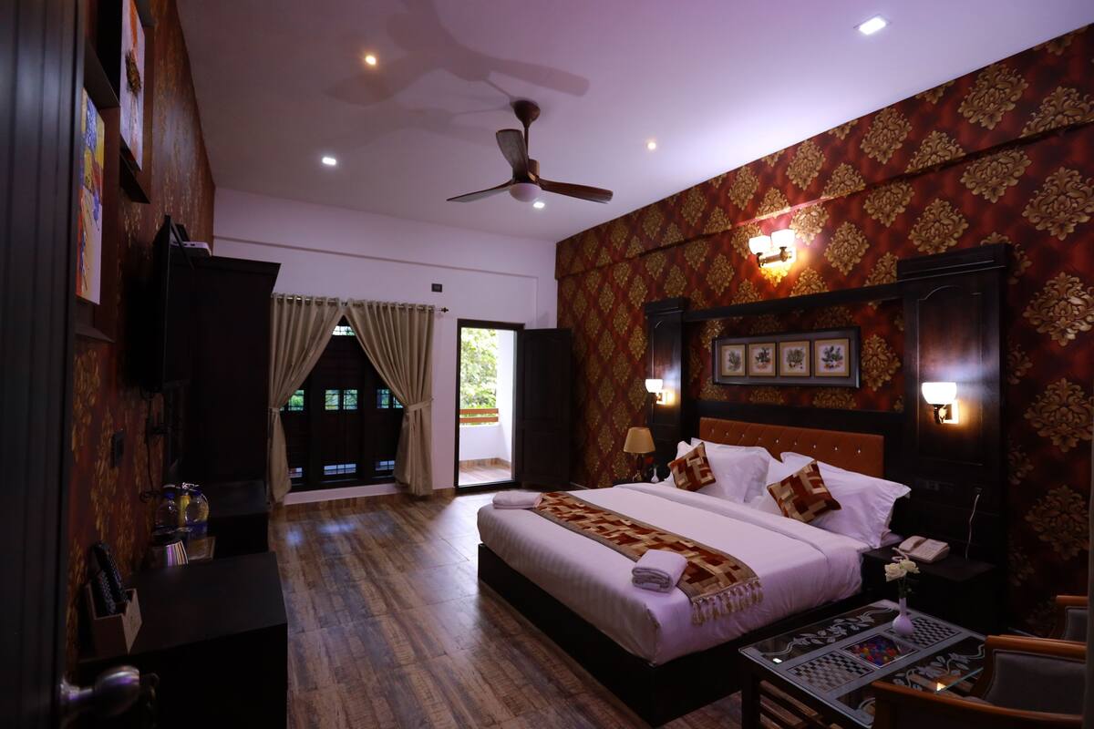 A hotel room with a bed, bedside table, lamp, and a view of the outside.