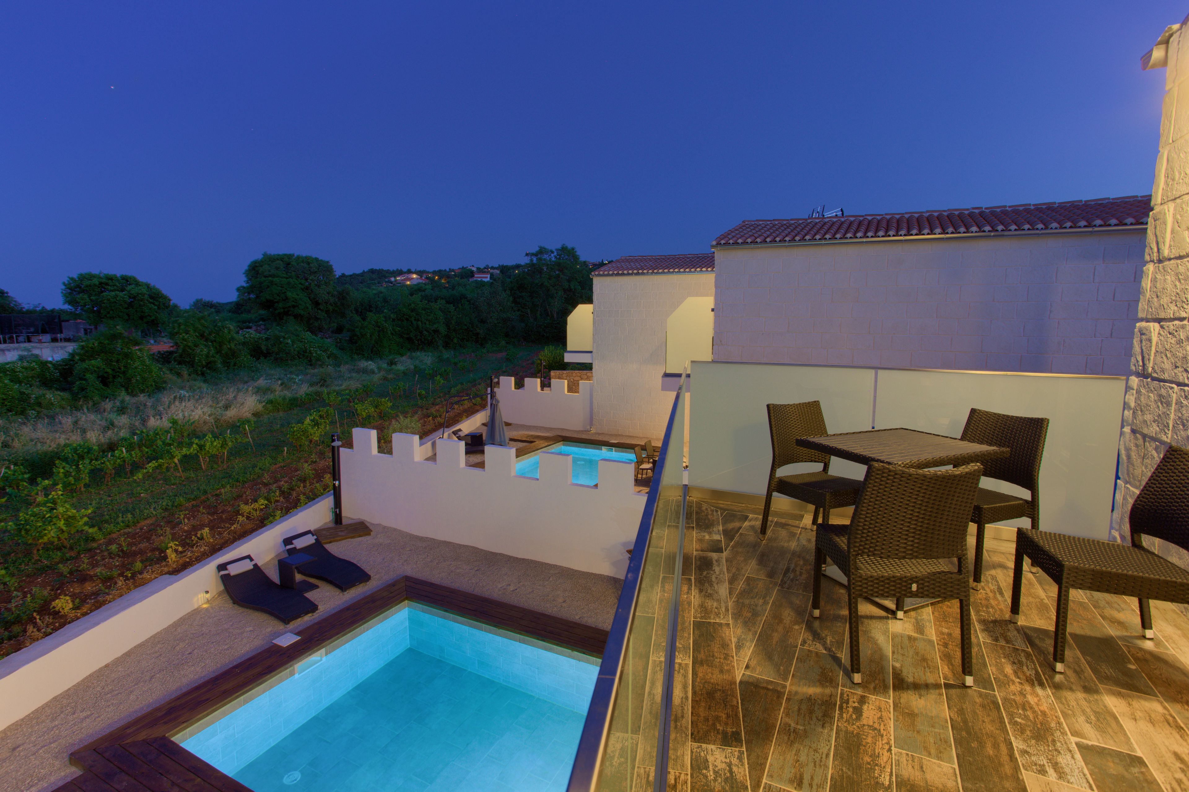 Un espace piscine aménagé sur le toit, avec une table et des chaises, entouré d’un petit muret et offrant une vue sur le paysage.