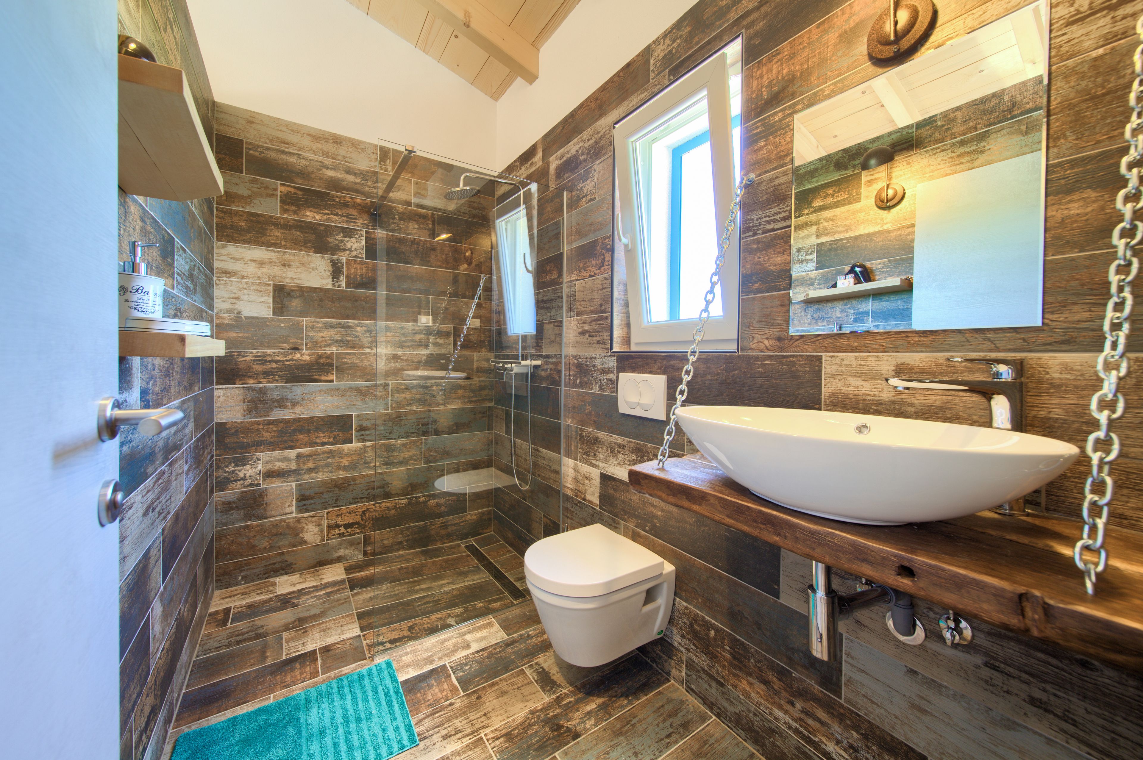 Ein modernes Badezimmer mit Holzboden, einem weißen Waschbecken und einer Glasdusche.