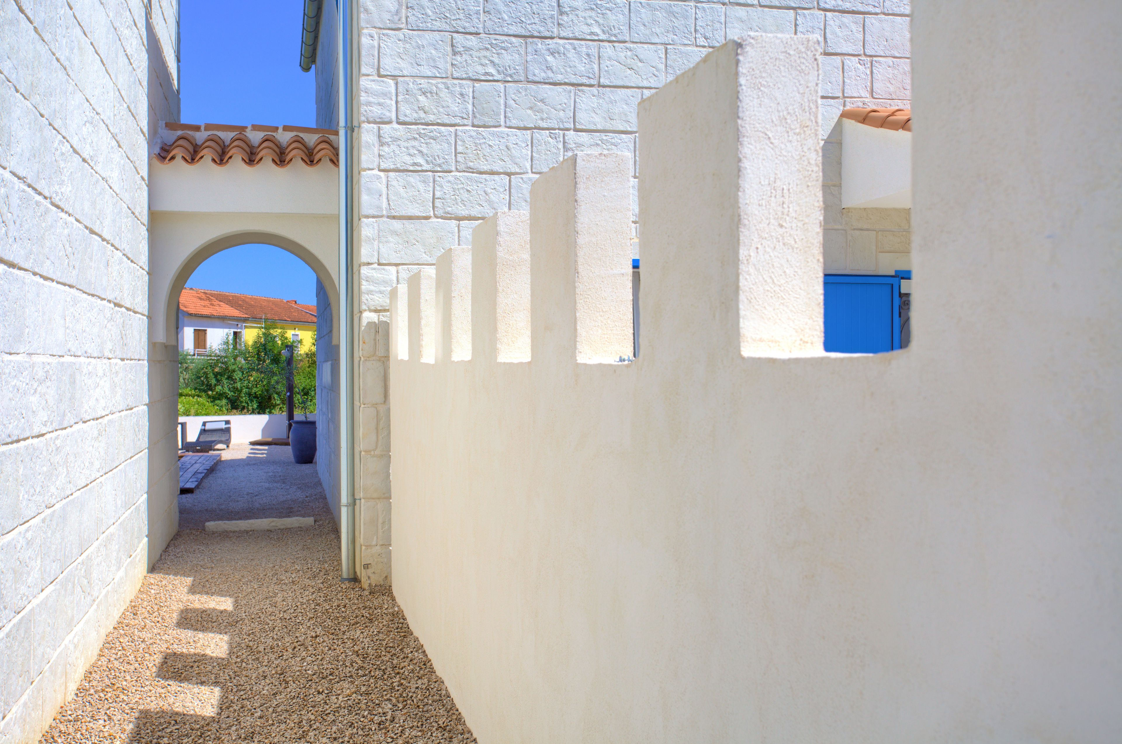 A narrow pathway with a tiled roof, white walls, and a blue door.