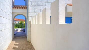 A narrow pathway with a tiled roof, white walls, and a blue door.