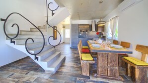 A spacious kitchen with a dining area, a staircase with ornate metal railings, and a modern air conditioning unit. - Pax House 1 (Krk)