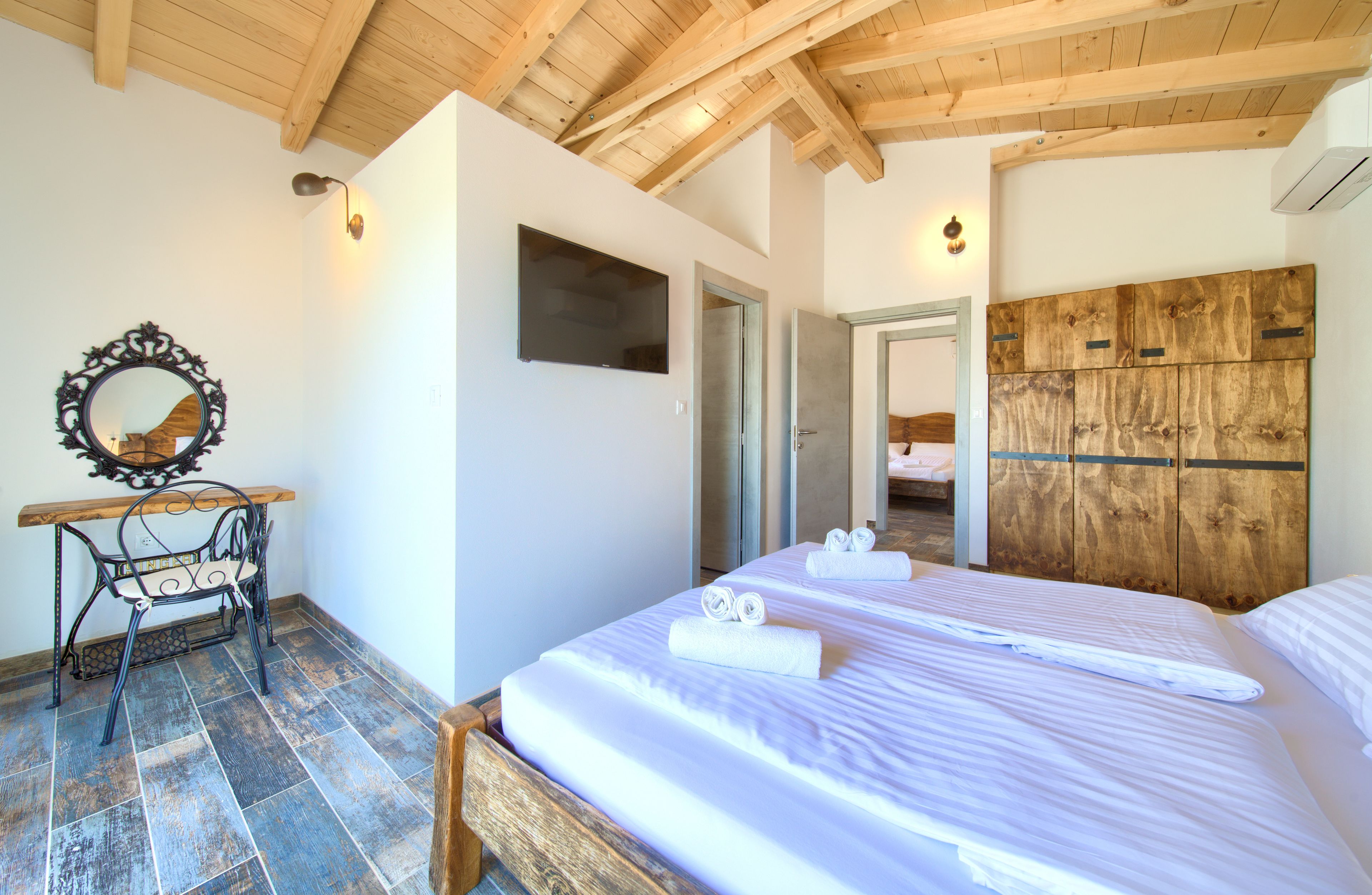 A bedroom with two beds, a wooden ceiling, a mirror, and a wooden wardrobe.