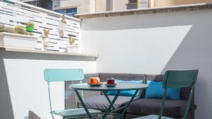 A balcony with a wicker sofa, two green chairs, and a small table with a red cup.