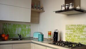 A modern kitchen with a gas stove, a sink, and a toaster. There are jars on a shelf above the stove and a word cloud on the wall.
