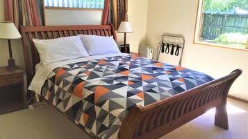 A bedroom with a wooden bed, a patterned bedspread, a nightstand with a lamp, and a window with curtains.