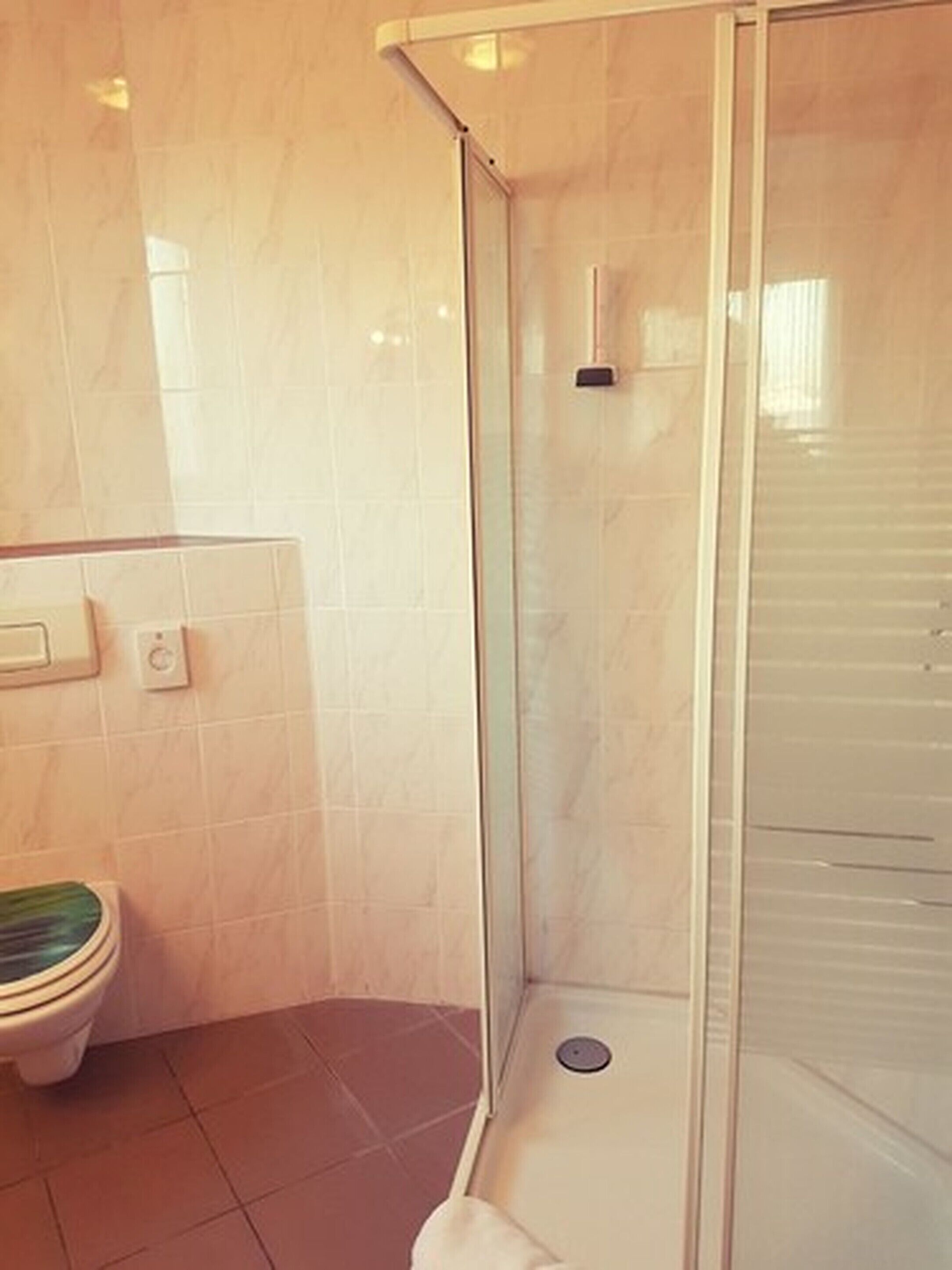 Une salle de bain avec une douche à parois de verre, des toilettes et un luminaire fixé au mur.