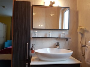 A bathroom with a large mirror, a white sink, and a hairdryer mounted on the wall. - Legend (Biebesheim am Rhein)