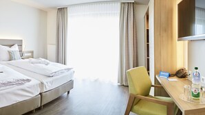 Een hotelkamer met een tweepersoonsbed, nachtkastjes, een bureau met een stoel, een televisie en een waterfles op het bureau.