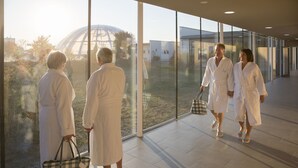 Een moderne hotelentree met grote ramen, een zichtbare glazen koepelstructuur buiten en een ruime, betegelde vloer.
