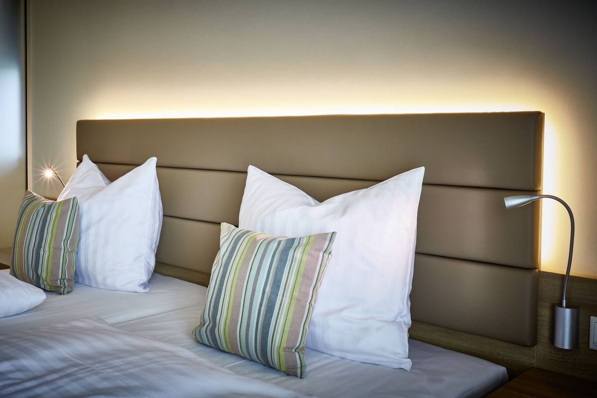 Een hotelkamer met een bed, twee kussens, een hoofdbord en een bedlamp.