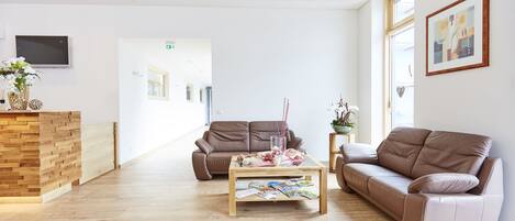 Ein moderner Empfangsbereich mit einem Holztresen, zwei Sofas, einem Couchtisch mit Zeitschriften und einem großen Fenster.