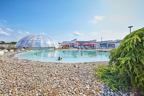Une piscine entourée de galets, une structure en forme de dôme transparent et des parasols rouges.