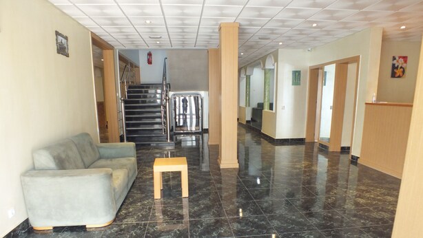 A lobby with a grey sofa, a wooden table, and a staircase leading to upper floors.