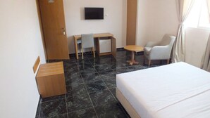 A hotel room with a bed, a desk with a chair, a television, and a small table.