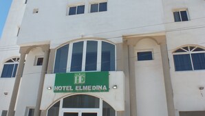 A white building with a green sign reading "HOTEL ELMEDINA" above the entrance.