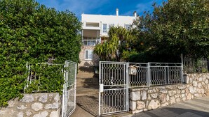 A gated entrance with a stone wall and metal gate, leading to a white building with balconies. - Bovolini's Place (Dubrovnik)
