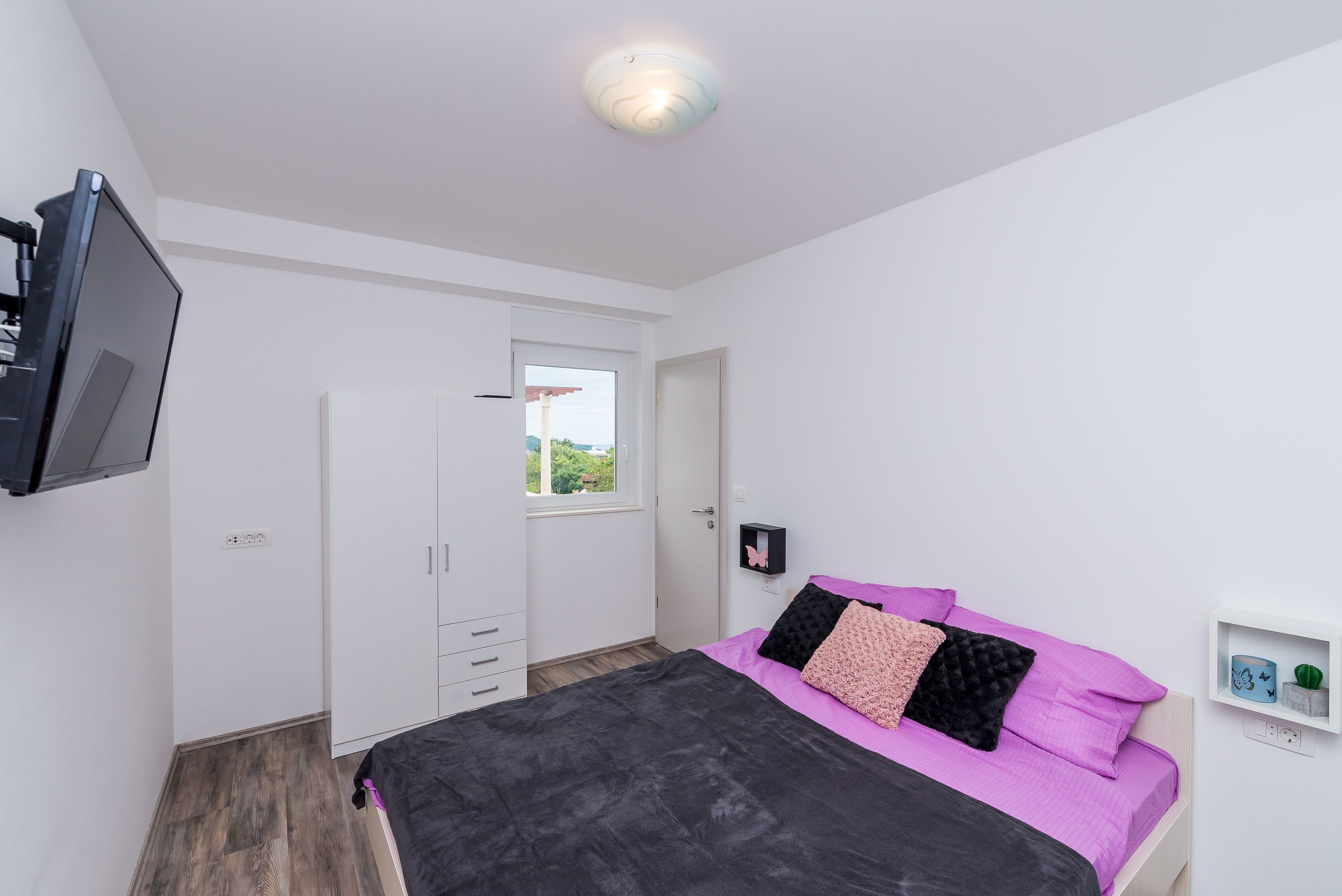 A bedroom with a bed, a wardrobe, a television, and a window.
