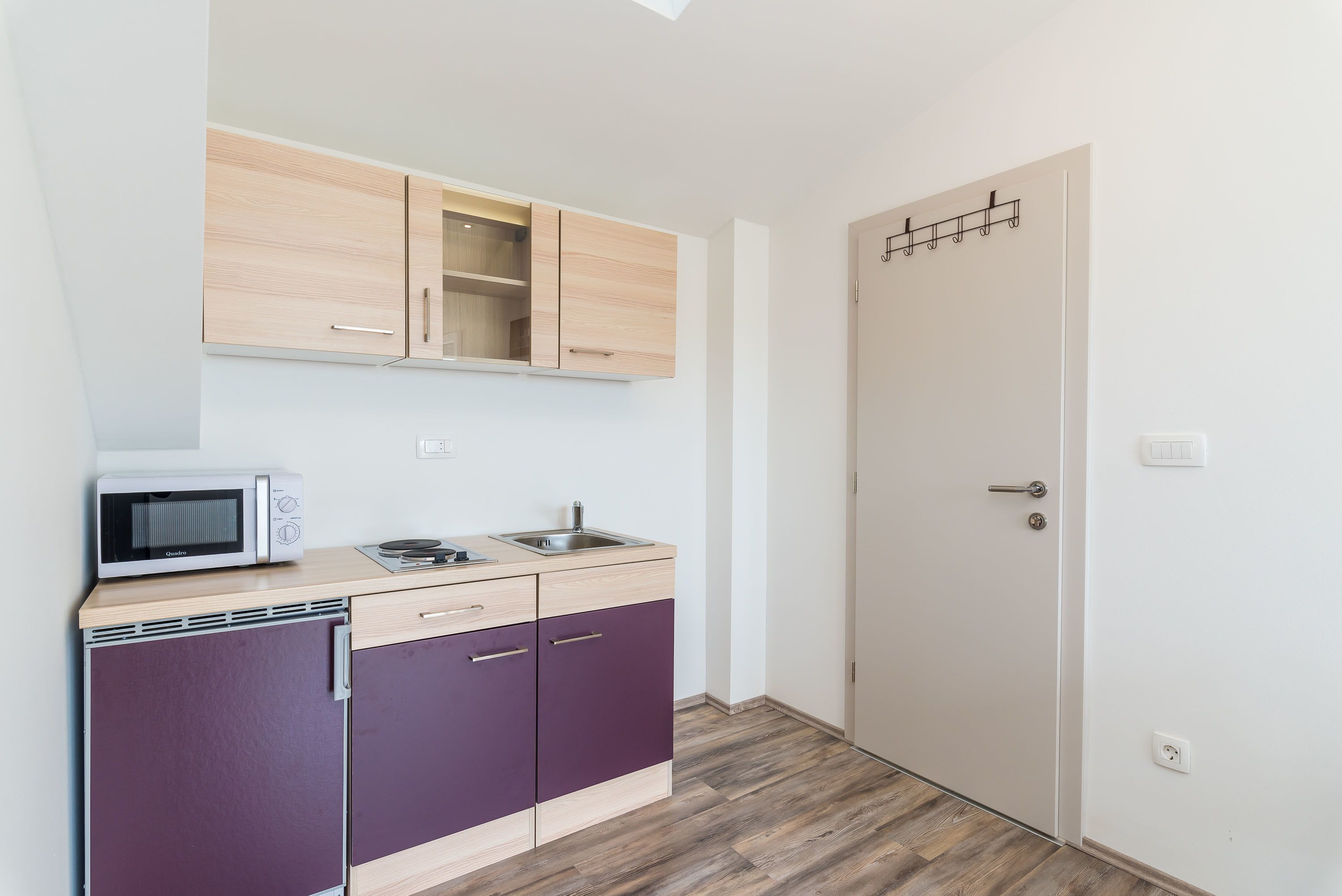 A compact kitchen with a microwave, sink, and wooden cabinets.