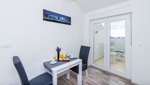A modern dining area with a table set for two, a cityscape artwork on the wall, and a sliding glass door leading to an outdoor balcony. - Bovolini's Place (Dubrovnik)